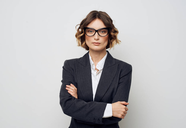 Uma mulher de negócios em óculos e em um terno em um fundo leve cruzou os braços sobre o peito - Foto, Imagem