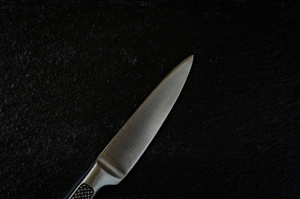 Λαμπερό ανοξείδωτο ακόμα μαχαίρι κουζίνας τοποθετείται σε ανάγλυφη μαύρη πέτρα - Φωτογραφία, εικόνα