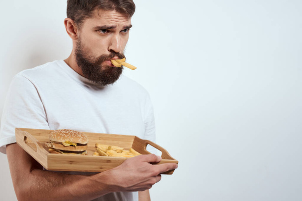 férfi fa tálca sült krumpli és hamburger gyorsétterem kalória modell fehér póló - Fotó, kép