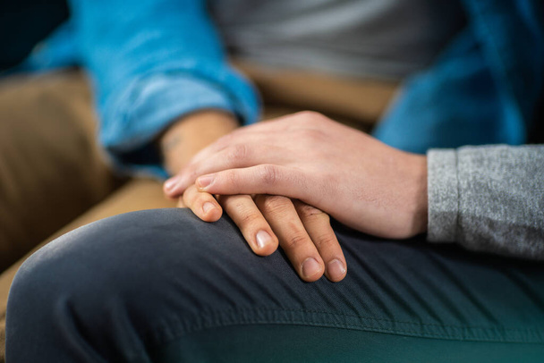 Close-Up of a Gentle Male Gay Couple Sitting Together on a Sofa at Home. Boyfriend Puts His Hand on Partners. They are Casually Dressed and Their Room Has Modern Interior. - Photo, image