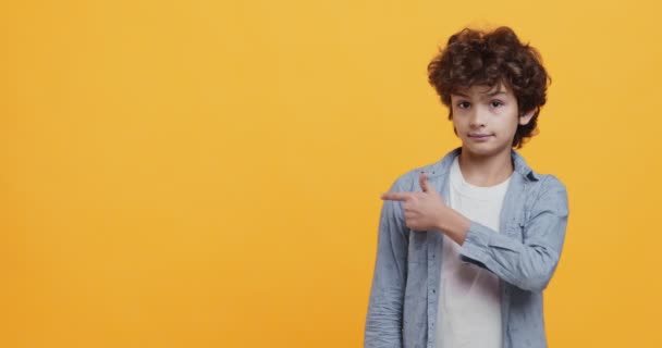 Podívej. Roztomilý kudrnatý chlapec ukazuje prstem na prázdné místo a přikyvující, oranžové studio pozadí - Záběry, video