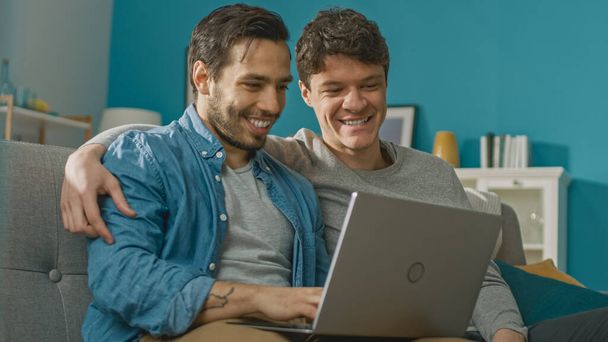 Sweet Male Gay Couple Spend Time at Home. They Sit on a Sofa and Use the Laptop. They Browse Online. Partners Hand is Around His Lover. Room Has Modern Interior. - Fotoğraf, Görsel