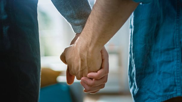 Close Up of Two Male Hands Gently Touching and Holding Each Other. Cute Queer Relationship Concept. Gay Couple are Casually Dressed. Room is Bright and Sunny. - Foto, afbeelding