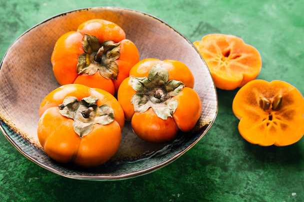 persimmon in a ceramic plate on a green background - Foto, afbeelding
