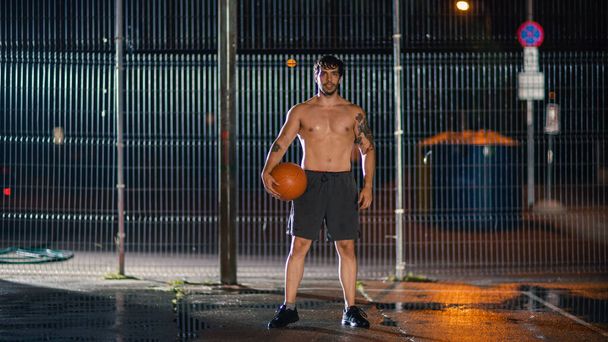 Athletic Young Male Basketball Player Sranding with the Ball in Crouched Position in a Residential Neighborhood Fenced Streetball Court. - Foto, imagen