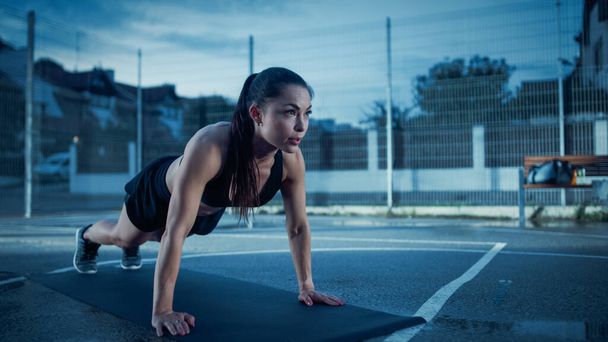 Beautiful Energetic Fitness Girl Doing Push Up Exercises. She is Doing a Workout in a Fenced Outdoor Basketball Court. Evening Shot After Rain in a Residential Neighborhood Area. - Foto, Bild