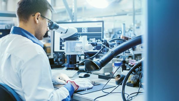 Electronics Factory Worker in White Work Coat Inspects a Printed Circuit Board Through a Digital Microscope. High Tech Factory Facility. - Foto, Bild