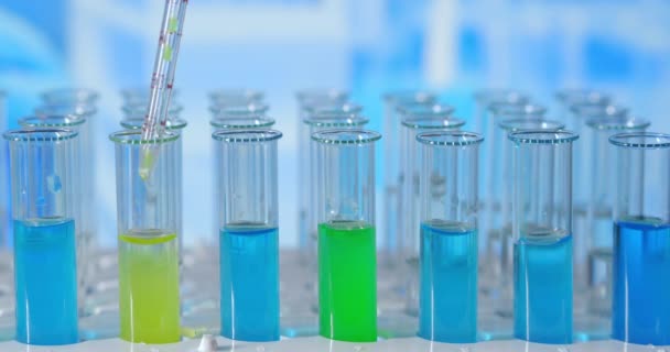 Wetenschapper injecteert chemicaliën in reageerbuizen. Testbuis met gekleurde vloeistof op de laboratoriumtafel op de achtergrond van de glazen kolven. gegoten van glazen pipet in reageerbuis verlicht met blauw licht - Video