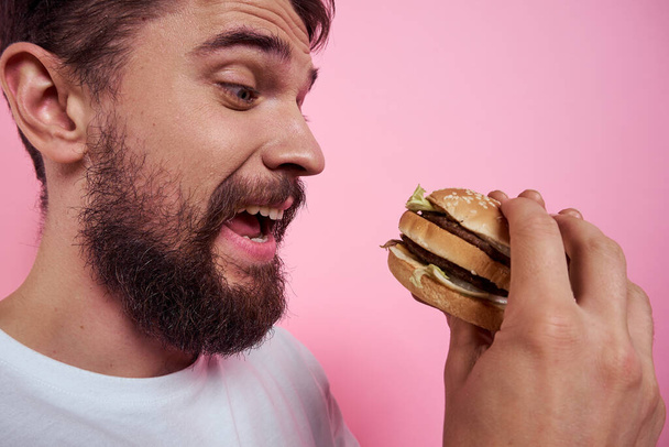 Portrait of a man with a hamburger on a pink background close-up cropped view of a model - Photo, Image