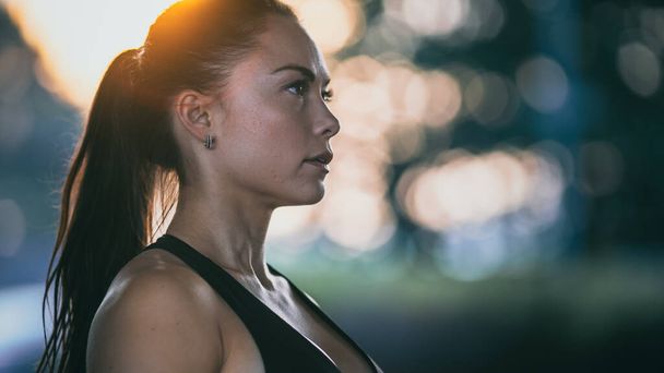 Portrait Shot of a Beautiful Confident Fitness Girl in Black Athletic Top on a Street. She is a Brunette with Brown Eyes with Her Hair Tied in an Ponytail. Shot is Taken in an Urban Environment. - Foto, afbeelding