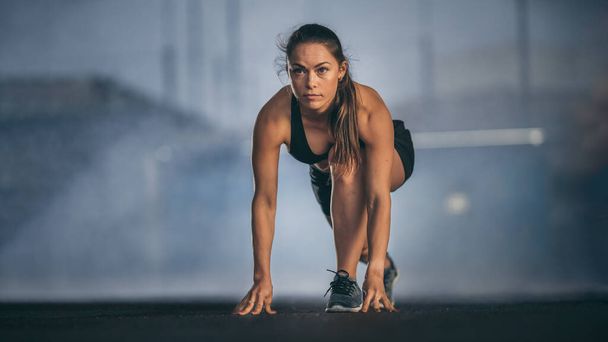 Beautiful Strong Fitness Girl in Black Athletic Top and Shorts Ready for Start Sprint. She is in an Urban Environment Under a Bridge with Foggy Background. - Photo, Image