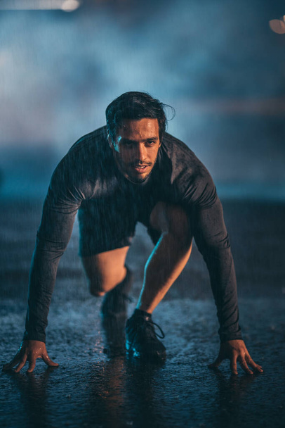 Strong Muscular Fit Young Man Ready for Sprinting on a Rainy Evening. He is Training in an Urban Environment Under a Bridge with Dark Foggy Background. - Foto, afbeelding
