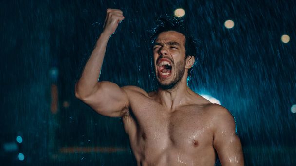 Shirtless Athletic Muscular Young Man is Celebrating His Sport Accomplishments on a Rainy Night. He is in an Urban Environment Under a bridge with Cars in the Background. - Fotoğraf, Görsel