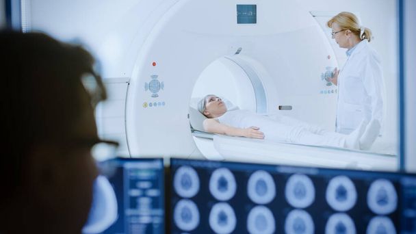In Medical Laboratory Patient Undergoes MRI or CT Scan Process under Supervision of Radiologist, in Control Room Doctor Watches Procedure and Monitors with Brain Scans Results. - Foto, Imagem