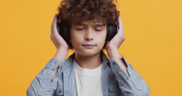 Крупним планом студійний портрет кучерявого хлопчика, який насолоджується музикою у великих бездротових навушниках
 - Кадри, відео
