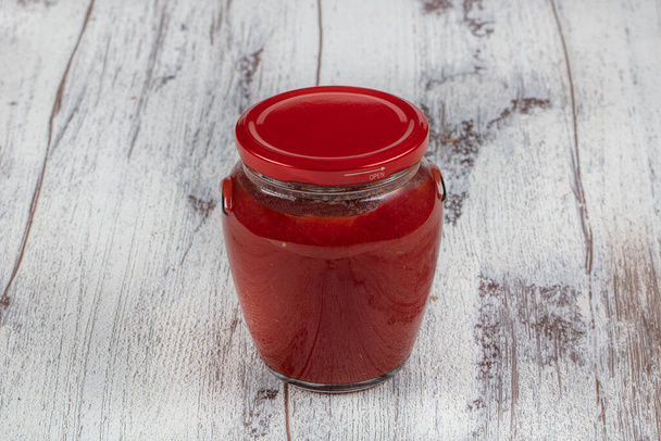 Pomidory we własnym soku lub pasta pomidorowa w szklanym słoiku na białym drewnianym stole. Przestrzeń kopiowania. - Zdjęcie, obraz