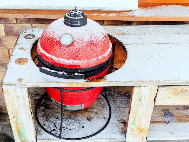 Punainen keraaminen BBQ grilli kevyesti pölytetty lunta reikä puupöydän - Valokuva, kuva