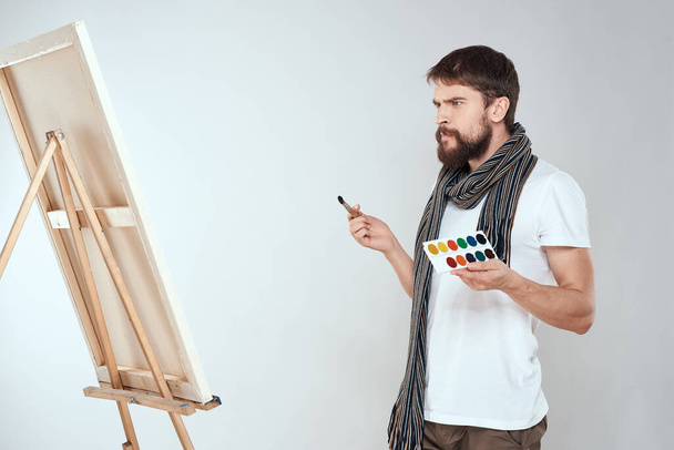 Чоловік художник малює на мольберті пензлем і малює в руках хобі креативність світлого фону
 - Фото, зображення
