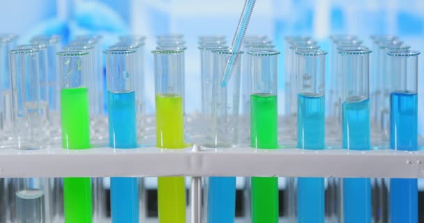 Лаборант добавляет зеленую жидкость в пробирку, контролирует химическую реакцию. Техник тщательно капает раствор из пипетки в стеклянные трубки для анализа ДНК. Фармацевтическая лаборатория - Кадры, видео