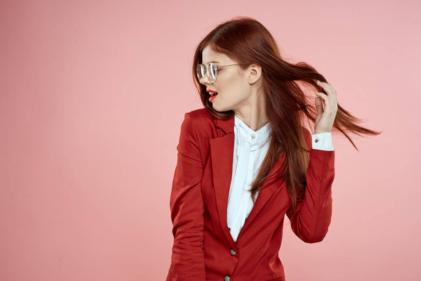 Nainen punaisessa takissa lasit punaiset huulet pitkät hiukset vaaleanpunainen tausta - Valokuva, kuva