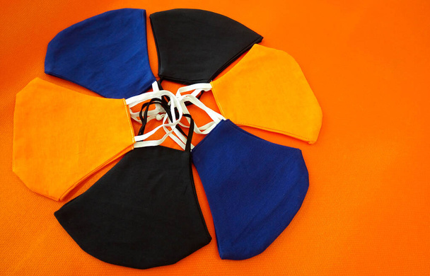 Понятие ручной работы. Top view, face masks made of cotton fabric on an orange background. Многоразовые защитные маски. кашель, пыль, вирус, бактерии, COVID-19. - Фото, изображение