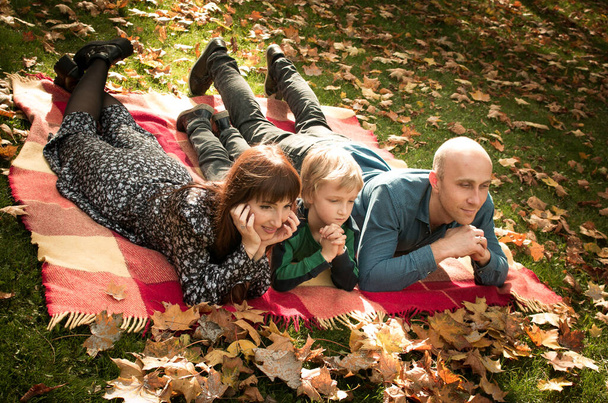 Caída. Familia feliz - mamá, papá e hijo durante un paseo por el parque de otoño. Concepto de emoción. El niño y sus padres están de buen humor.. - Foto, imagen
