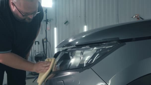 Service worker polishes headlights apron optics with microfiber towel after restoration polishing. Car detailing concept - Footage, Video