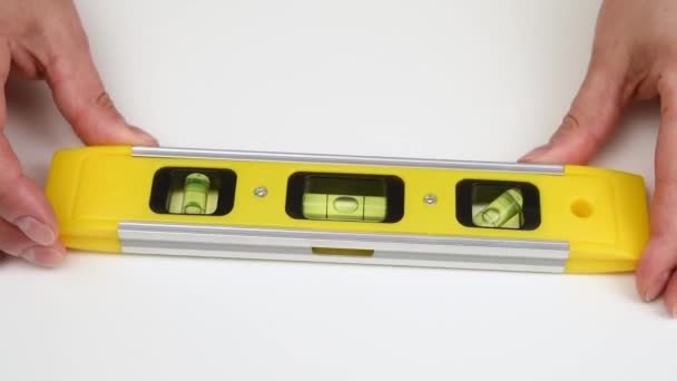 mano femminile tenendo un livello di plastica gialla per la costruzione su uno sfondo bianco, primo piano - Filmati, video