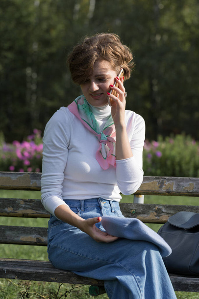 Young woman in the park speaks by mobile phone. Cute girl portrait in french style. - Foto, afbeelding