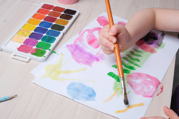 the child draws with a brush on paper, drawing with watercolors at the table, creativity for children, development of imagination in children - Photo, image