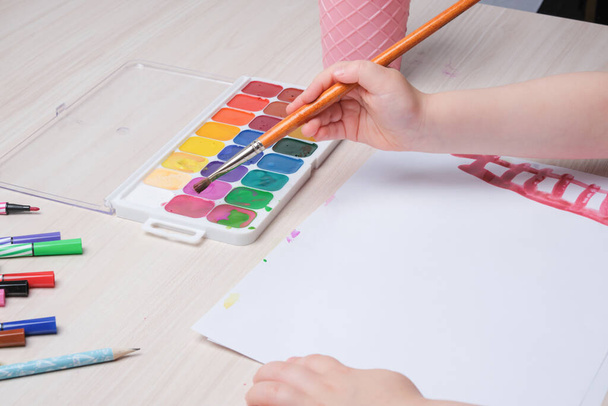 the child draws with a brush on paper, drawing with watercolors at the table, creativity for children, development of imagination in children - 写真・画像
