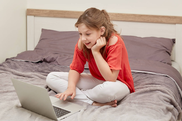 Happy girl sitting on the bed, looking at an open laptop. - Valokuva, kuva