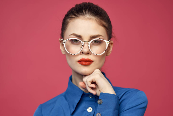 Gözlüklü ve mavi gömlekli bir kadının portresi. Kırmızı dudaklı, pembe arka plan modeli. - Fotoğraf, Görsel
