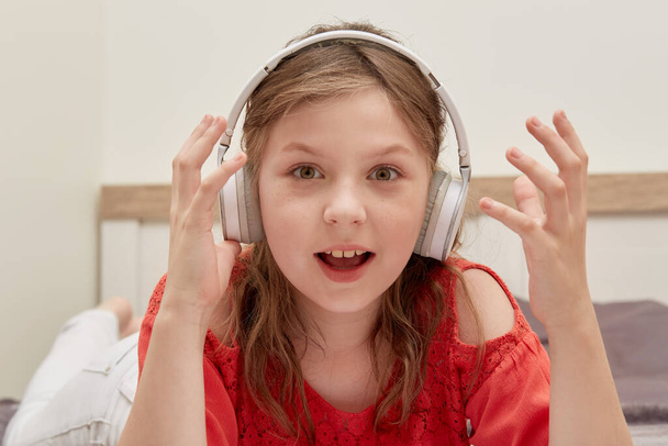 Girl with headphones listening to music and lying in bed, looking at the camera. - Foto, imagen