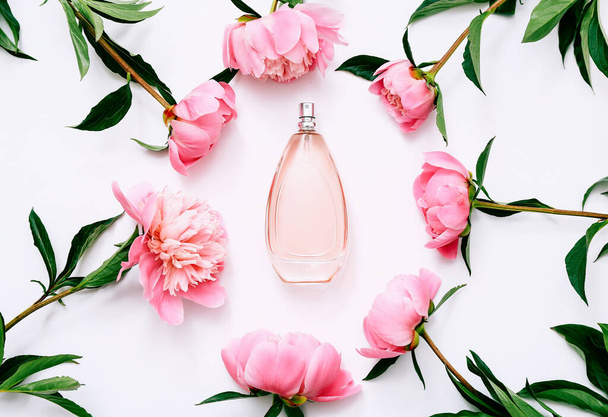 Botella rosa de perfume de mujer y flores de peonía sobre fondo blanco. Fragancia suave primavera para las mujeres. Vista superior, plano - Foto, imagen