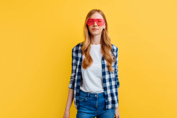 young woman in casual clothes and pink glasses on a yellow background - Fotoğraf, Görsel