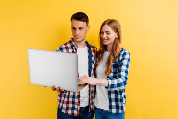 young man and woman in a plaid shirt, using the laptop on a yellow background - Valokuva, kuva
