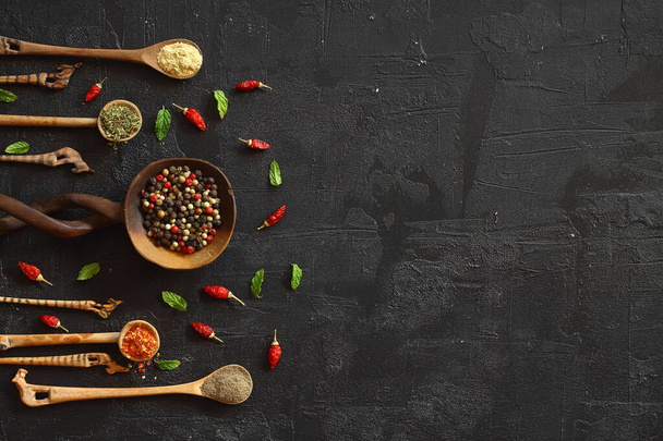 Different kind of spices on a black stone. Oriental spices in spoons, peppers, curry powder, herbs on black metallic tray in Asian style. Flat lay, top view. - Фото, зображення