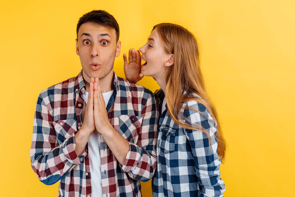 young people, man and woman, woman whispering a secret in the ear of a man, gossip on yellow background - Foto, afbeelding