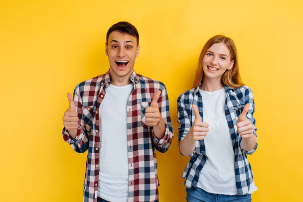 young couple of friends, man and woman, showing thumb up gesture on yellow background - Fotografie, Obrázek