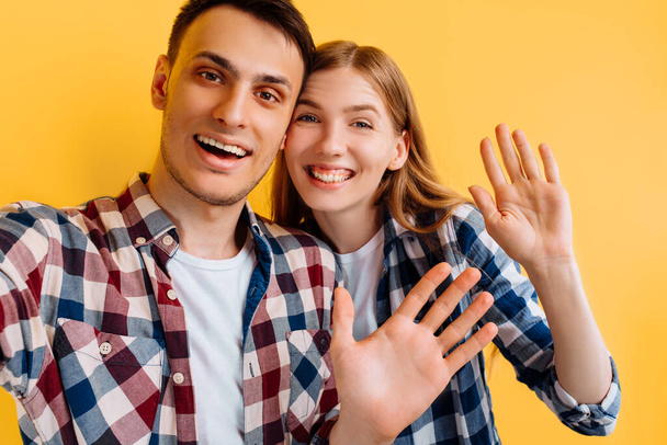 cheerful couple, man and woman make selfie on mobile phone on yellow background - Foto, imagen
