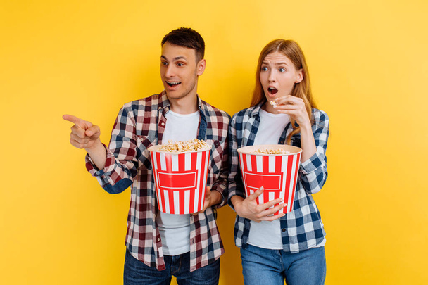 man and woman eating popcorn while watching movie on yellow background - Фото, зображення