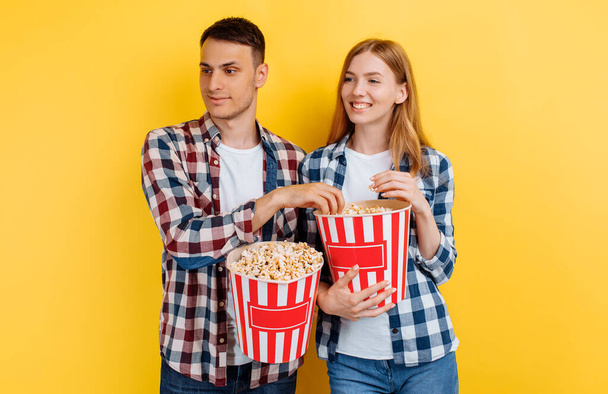 Shocked couple, man and woman with popcorn on yellow background - Φωτογραφία, εικόνα