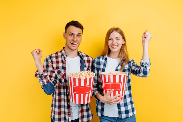 excited young couple watching movie with popcorn on yellow background - Valokuva, kuva