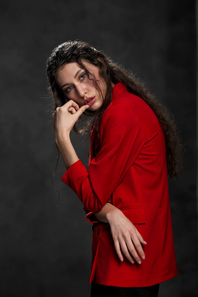 A young beautiful oriental woman with long black hair in a red jacket against a black background. The fashion model poses in the studio. - Photo, image