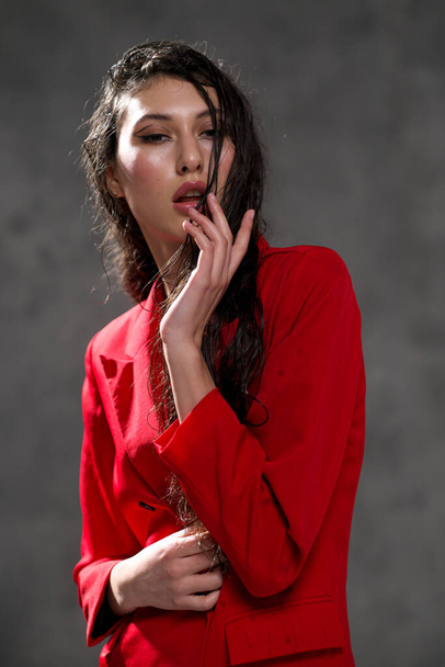 A young beautiful oriental woman with long black hair in a red jacket against a black background. The fashion model poses in the studio. - Photo, Image