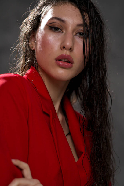 A young beautiful oriental woman with long black hair in a red jacket against a black background. The fashion model poses in the studio. - Valokuva, kuva