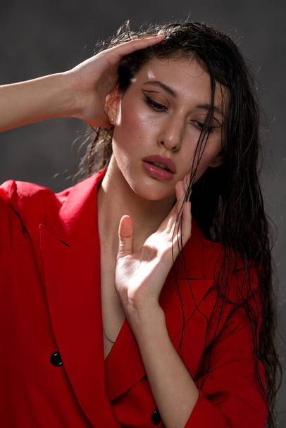A young beautiful oriental woman with long black hair in a red jacket against a black background. The fashion model poses in the studio. - Fotografie, Obrázek