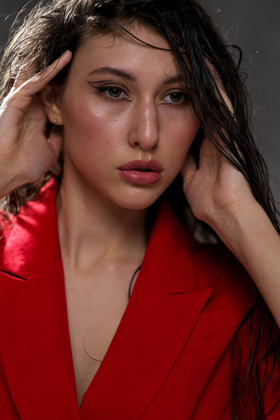 A young beautiful oriental woman with long black hair in a red jacket against a black background. The fashion model poses in the studio. - Foto, imagen