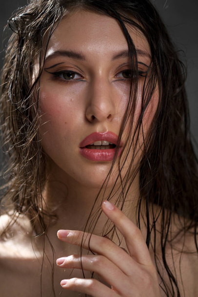 The face of a beautiful young girl with wet black hair close-up. Eastern appearance. Nude makeup, natural skin. - Foto, afbeelding